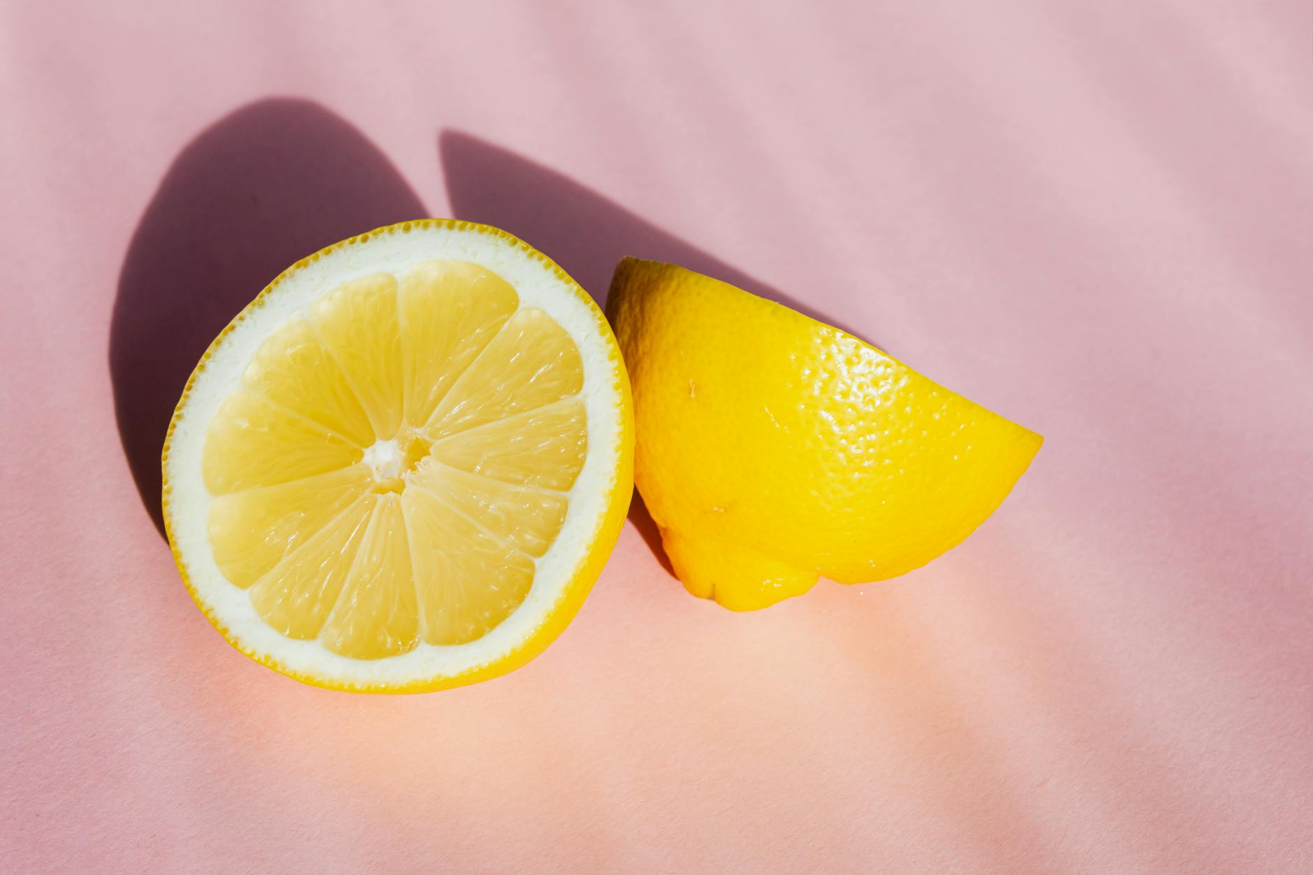 Halves of fresh lemon on pink background with sunlight