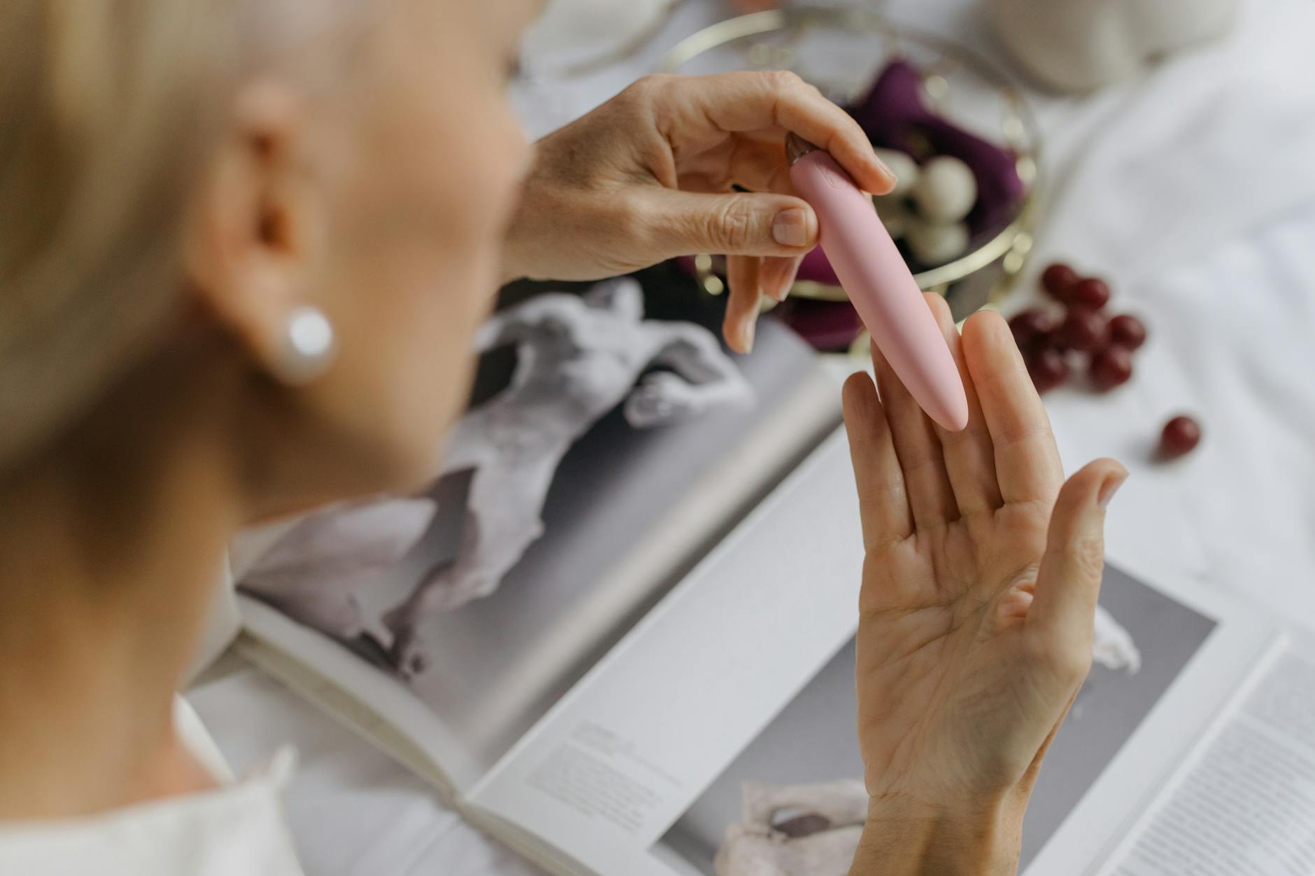 Close-up of a hand holding a pink vibrator with art books in soft focus background