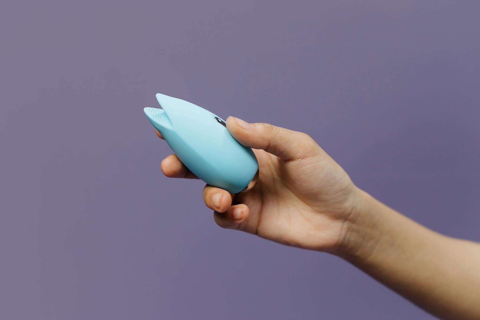 A blue silicone vibrator held in hand against a solid purple background, promoting self-love and sexuality.